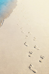 Foot prints of two people on sandy beach with wave, selective focus