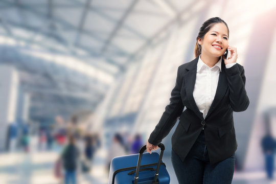 businesswoman talking on mobile phone while carrying luggage