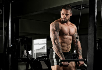 Fototapeta na wymiar Muscular bodybuilder guy doing exercises with dumbbells in gym