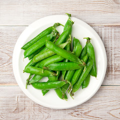 Green pea pods on the big white plate.