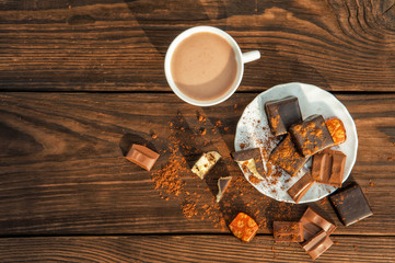 chocolate candies on plate and a cup with cocoa on wooden table. View from above