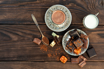 chocolate candies on plate and a cup with cocoa on wooden table. View from above