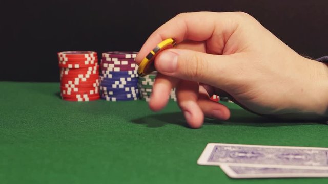 POKER: Player twirls a playing chip in the hand and thinks (side view)