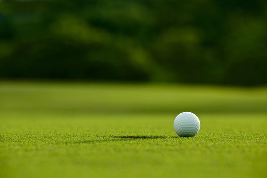 selective focus. white golf ball near hole on green grass good f