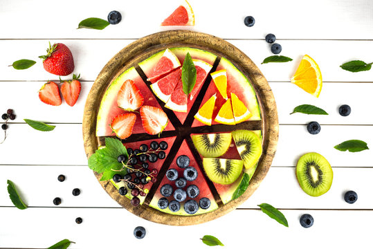 Sliced juicy watermelon pizza on white wooden table.  Watermelon, blueberries, grapefruit, orange,kiwi,strawberry,black currant,mint.Concept for healthy Eating. Eye bird view.
