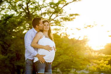 Fototapeta premium happy couple in love together in park landscape on sunset with woman pregnant belly and man