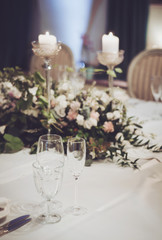 Wedding table set with classic chairs, floristics in banquet restoraunt. Floral composition beige, pink rose flowers, high candle coaster, glass goblets for wine on white tablecloth. Text, copy space