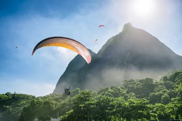Poster Paraglider passeert langs het mistige groen van de Pedra da Gavea-berg op weg naar de landing op het strand van São Conrado in Rio de Janeiro, Brazilië © lazyllama
