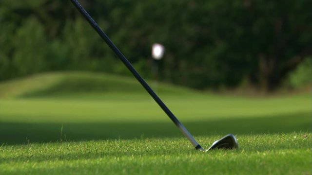 Close view of golf ball and club making a pitch shot, rack focus to ball bouncing onto green