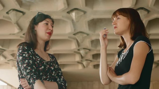 Two girls talking and smoking electronic cigarettes near the wall close-up