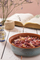 Light strawberry cake in a blue ceramic form on a white wooden background with old books and a bunch of flowers  