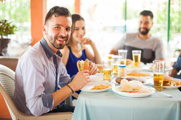 Handsome man eating hamburger with friends