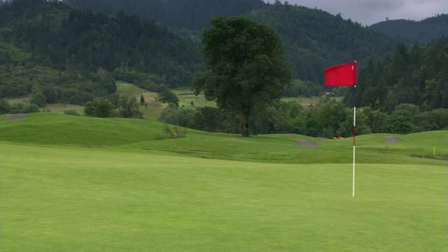 Red flag waving above hole on hilly golf course