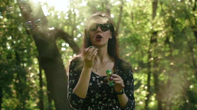 Cute girl with sunglasses blowing bubbles in the park with smoke slow-motion