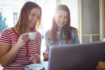 Happy friends using laptop at cafe