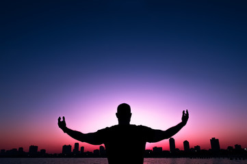 Silhouette of a man stretched out his hands, on background of sunset city