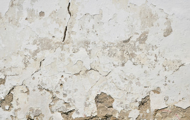 Old white painted plaster wall with cracks and stains