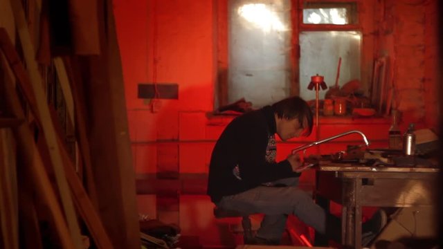 The artist paints a mask in a dark studio with a red light