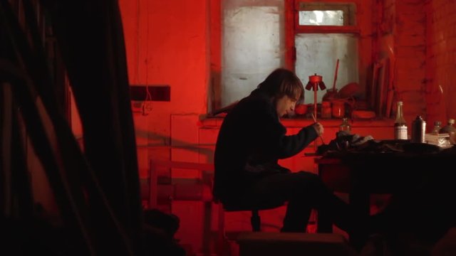 The artist paints a mask in a dark studio with a red light long shot