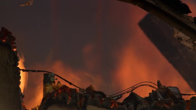 Behind smoldering siding, flames rage in the interior of a house gutted by fire