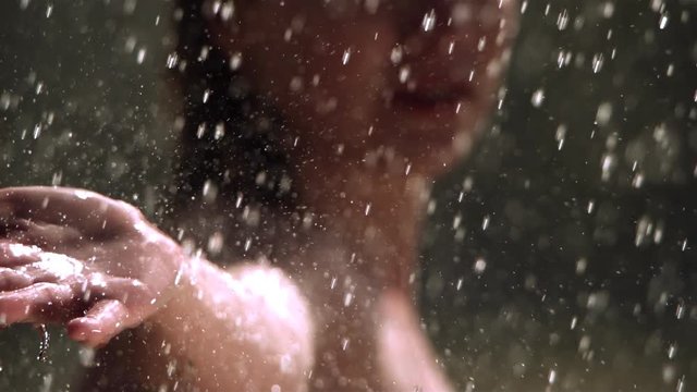 Soft focus close-up of woman's face and outstretched arm in ultra-slow motion rain