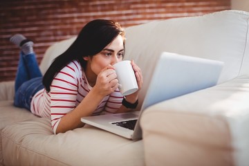 Woman drinking coffee while lying on couch