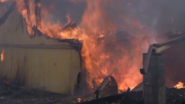 Flames consume collapsed rubble and the remaining portion of a wall in a house destroyed by fire