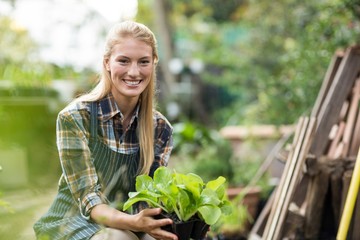 Smiling female gardener holding plant