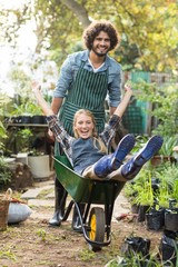 Cheerful man giving wheelbarrow ride to female gardener