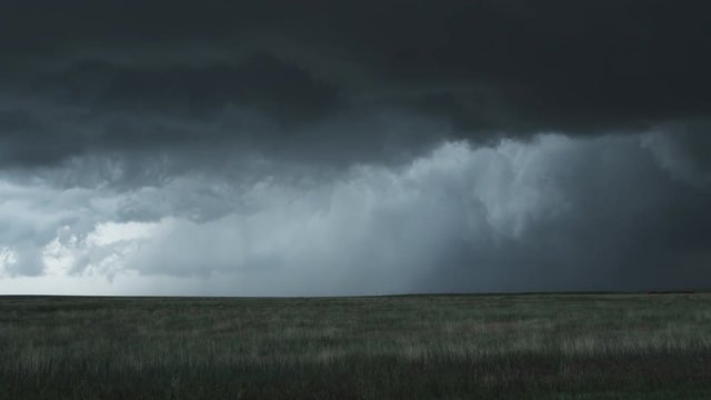 Lightning flashing below a wind-blown wall cloud rolling over grassland, time lapse