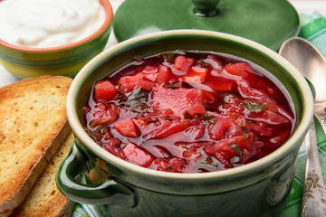 Borscht - traditional russian and ukranian beetroot soup in green ceramic pot on wooden background.