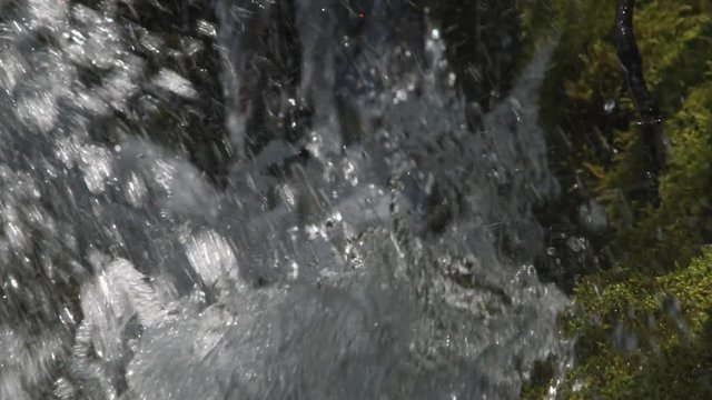 Slow-motion water drops splashing toward the camera from a mossy boulder in a stream