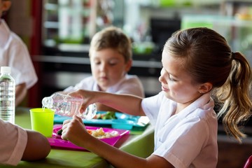 Obraz premium Schoolgirl pouring water in drinking glass