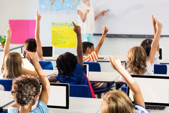 Teacher pointing students with raised hands in classroom