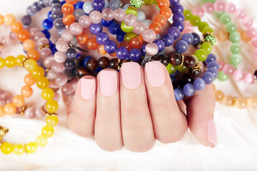 Hand with beige matte manicured nails and colorful bracelets
