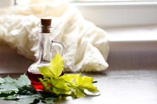 Maple syrup in glass bottle and maple leaves on dark wooden table