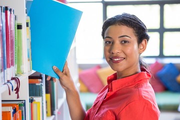 Smiling teacher removing book from bookshelf at library