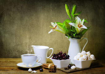 Still life with white lilies flower,hot tea,warm milk,sweet cherries,meringue and cinnamon on wooden table