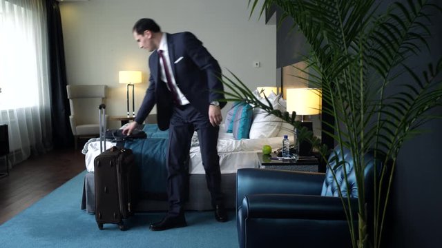 Businessman waiting for a taxi to the airport/Businessman sitting on a bed in a hotel room and glances at his watch. The taxi arrived, it's time to go to the airport