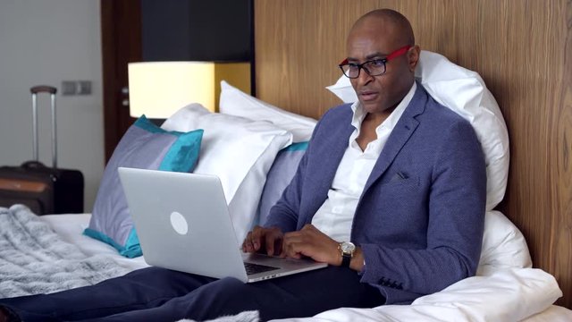 Businessman in Hotel Room/Businessman in a hotel room checks mail on a laptop. He feels himself comfortable on the bed and smiling from good news