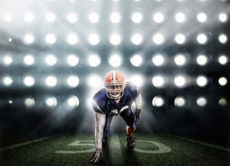 Young football player in blue uniform on background of spotlights