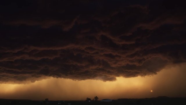Corrugated murky storm cloud hanging over a prairie farm at sunset, time lapse