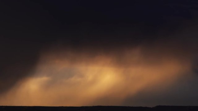 Dark clouds blow past followed by a clearing sky full of golden sunset clouds, time lapse
