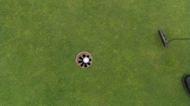 Golfer nudging ball with putter before sinking putt and retrieving ball from cup
