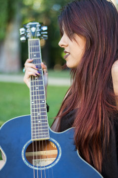 White girl holding the neck of the guitar while looking at the horizon. She was playing guitar in the park on a sunny summer day. 