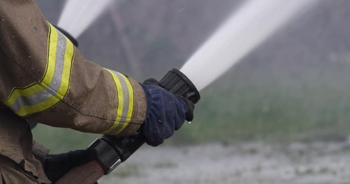 Firefighter's hands hold a streaming hose and raise the nozzle