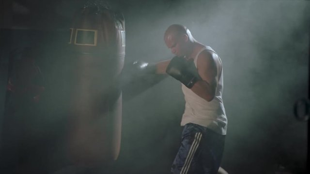 Shadowy figure climbing into a boxing ring in a steamy gym as camera pans to boxer punching a bag