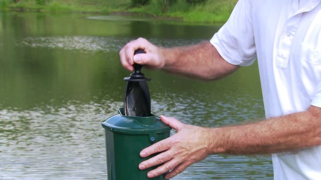 Man cleaning golf ball at ball washer near a pond