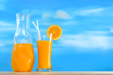 Orange juice in jug and glass on sky background