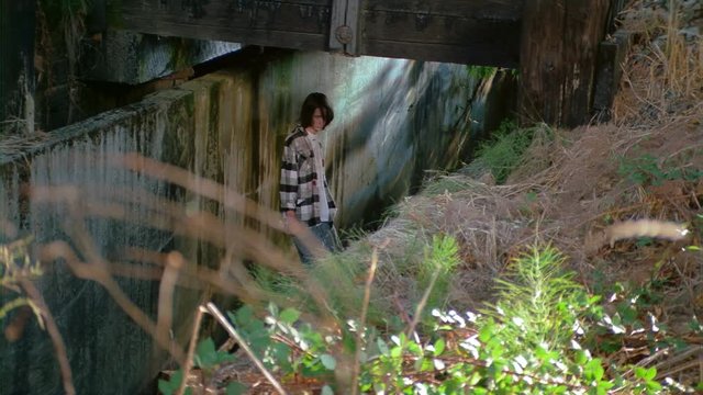 Dejected-looking teenage boy standing under a railroad trestle